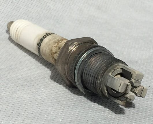 Pre-chamber plug off a biogas CHP engine — fouled electrodes and deposit through the chamber ports.