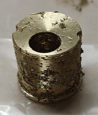 Threaded brass plug as machined — fine swarf bound to every thread and face by cutting oil.