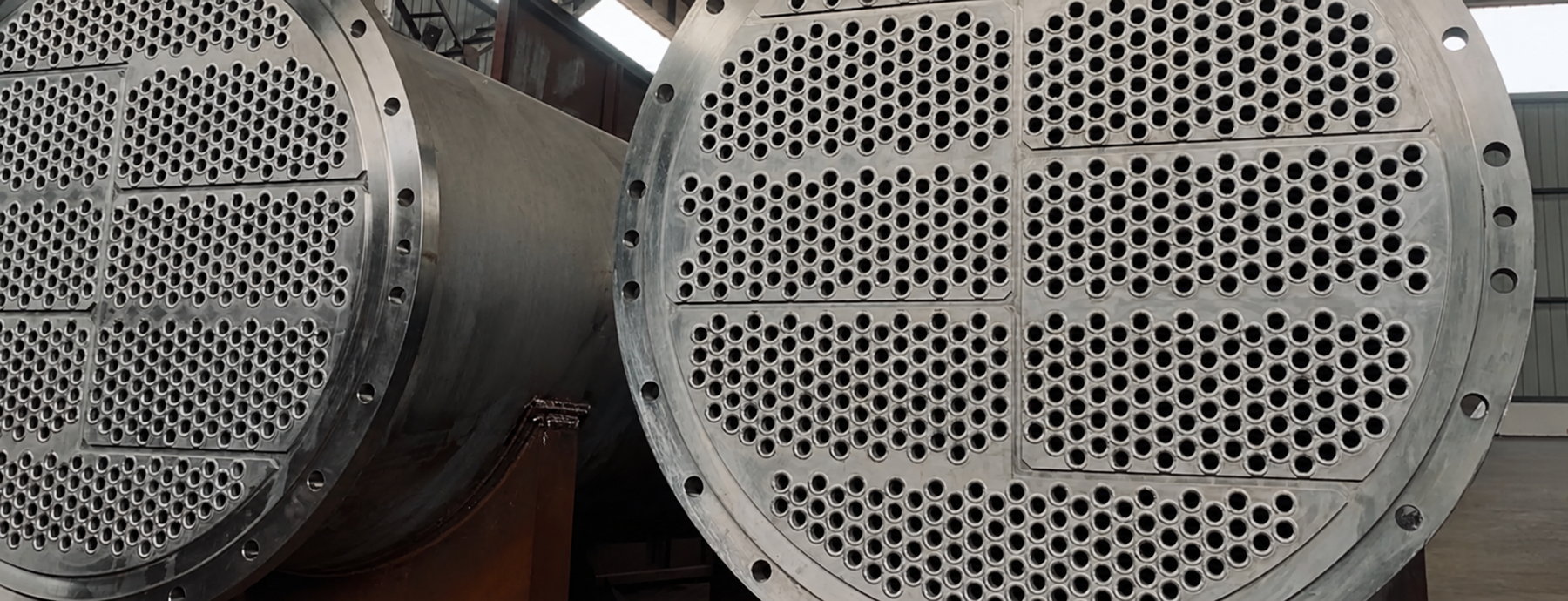 Two shell-and-tube heat exchanger bundles on a workshop floor, tube sheets and flanges facing the camera