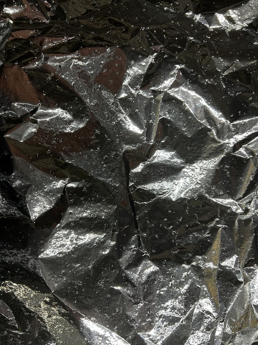 Close view of the same foil sheet showing dense pitting and gas bubbles held against the surface