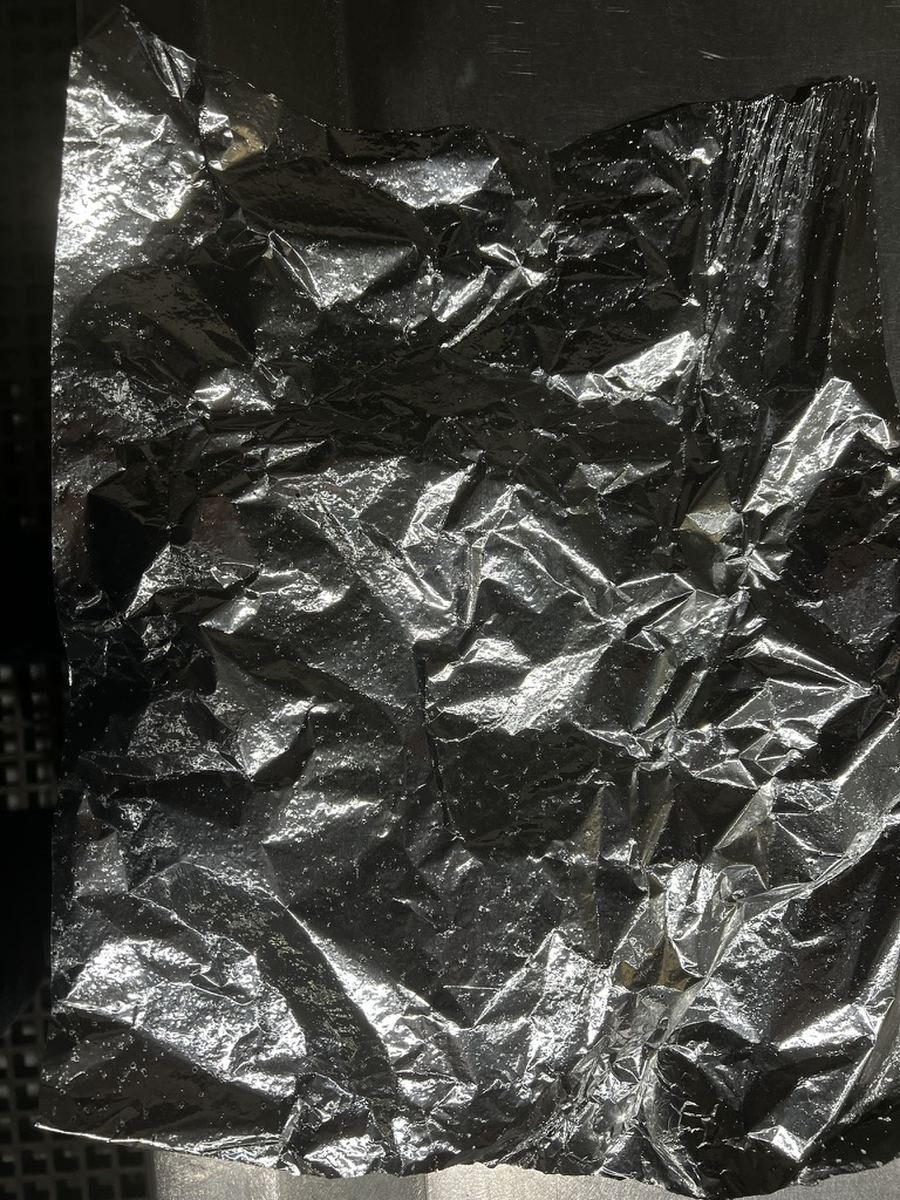 A foil test sheet lifted from a working ultrasonic bath and held against the tank wall, pitted across the whole face