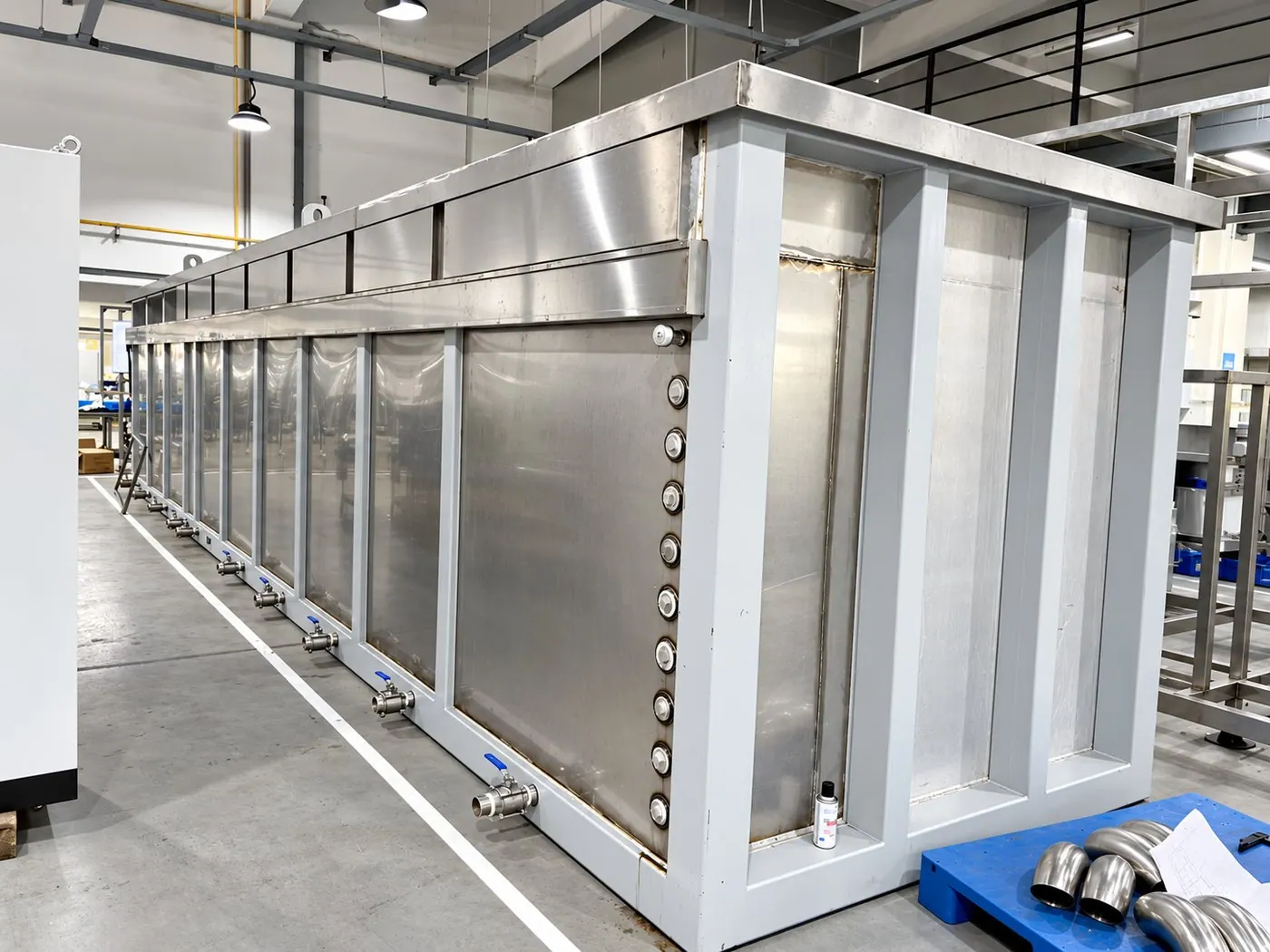 A Misonics UltraMax stainless steel ultrasonic tank under construction, showing the row of heater penetrations down the tank wall, the structural support frame and the drain valves along the base